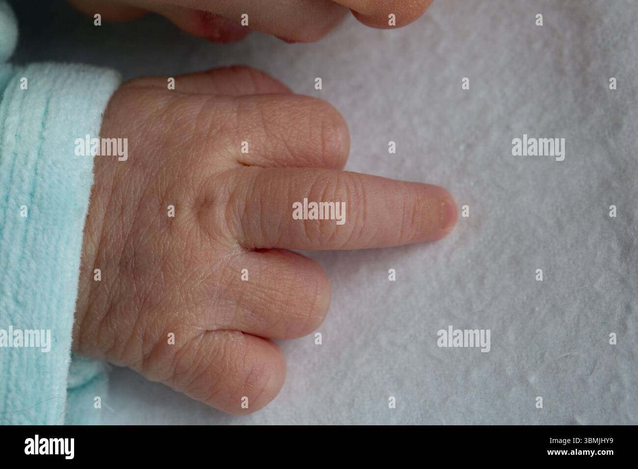 Kleine Neugeborene Hand, die sanft die Textur einer weichen weißen Decke erforscht, ein Moment friedlicher Entdeckungen Stockfoto