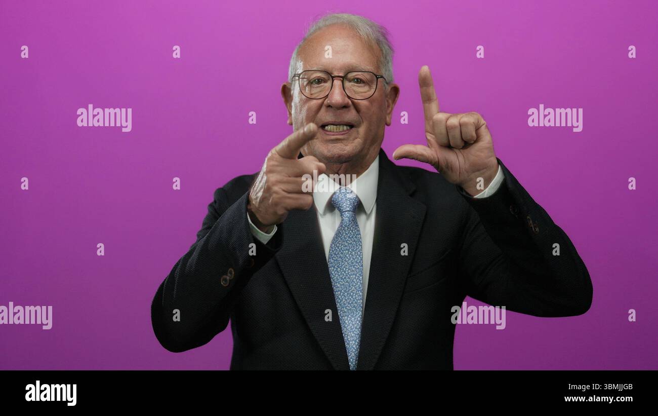 Senior Mann im Business-Anzug Gesten vor isoliertem rosa Hintergrund, der Konzept und Emotionen in ausdrucksstarken Posen ausdrückt. Stockfoto