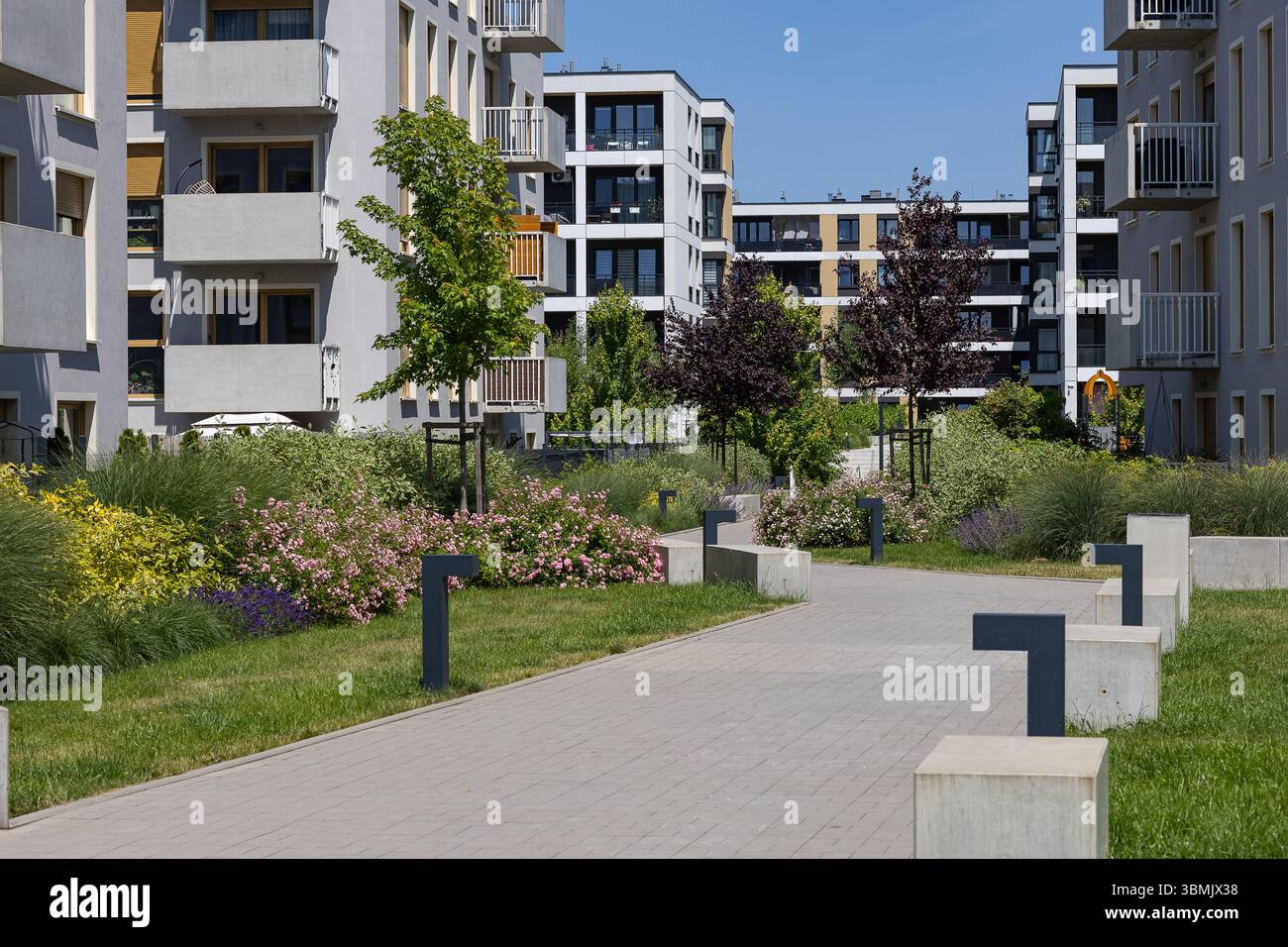 Moderne Wohngebäude mit begrüntem Innenhof, blühenden Blumenbeeten, grünen Bäumen und Wanderwegen. Städtische Wohnungs- und Außenraumgestaltung Stockfoto