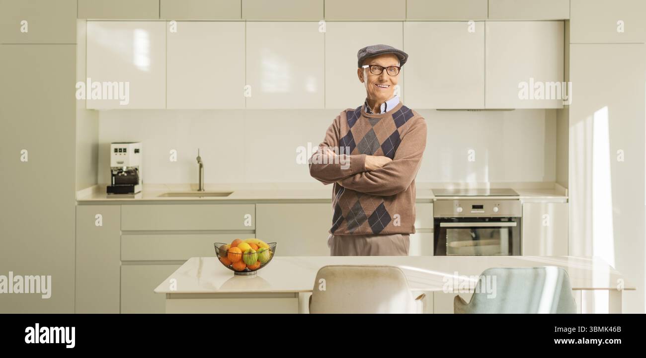 Lächelnder, lässiger älterer Mann posiert in einer Küche mit gekreuzten Armen Stockfoto