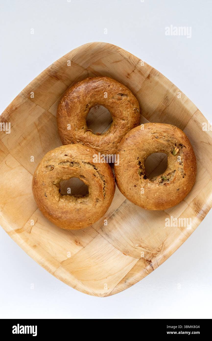 3 handgefertigte Bagels, traditionelle jüdische Brötchen in einer Holzschale auf einem weißen Schneidebrett Stockfoto