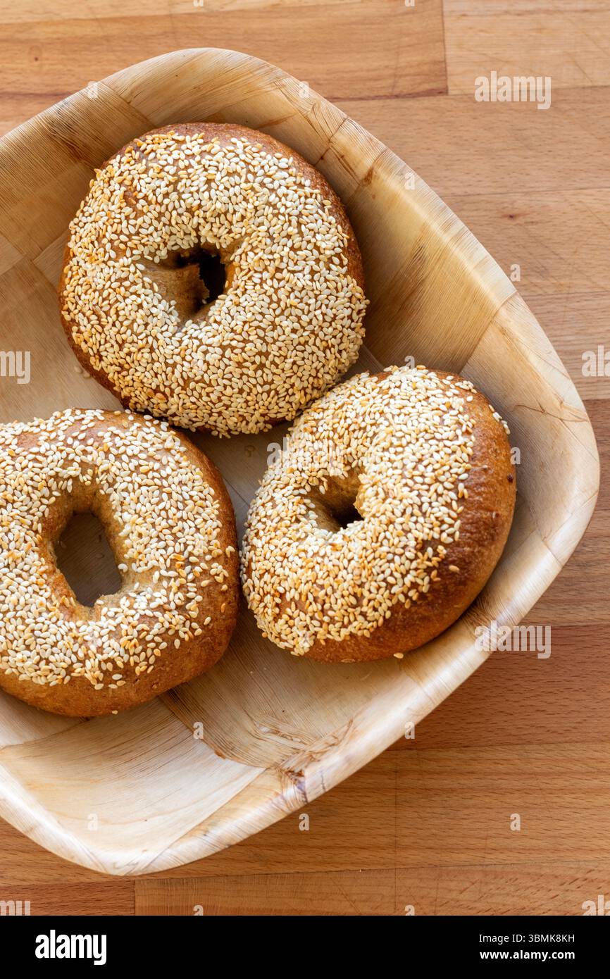 3 handgemachte Bagels mit Sesam-Samen, traditionelle jüdische Brötchen in einer Holzschale auf einem hölzernen Schneidebrett Stockfoto