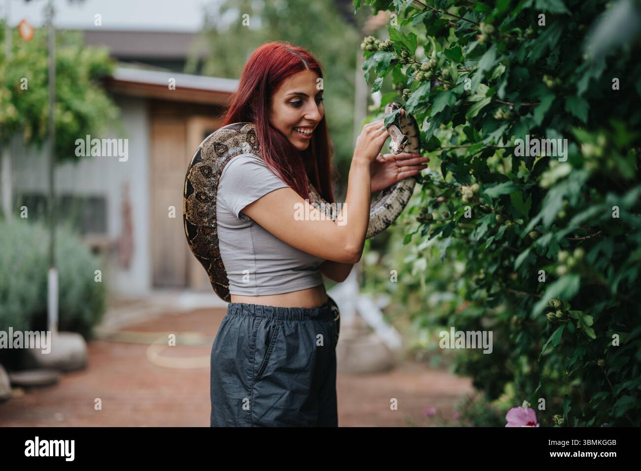Ein Mädchen hält draußen eine große Schlange in einem üppigen Garten Stockfoto