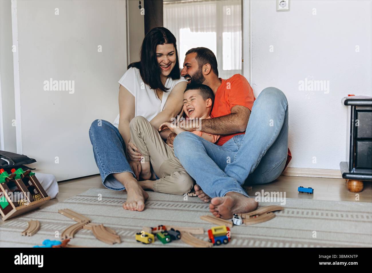 Mutter und Sohn spielen und lachen zusammen in einem gemütlichen Kinderzimmer. Sie kitzelt ihn, und beide genießen einen glücklichen, verspielten Moment voller Wärme, bondi Stockfoto