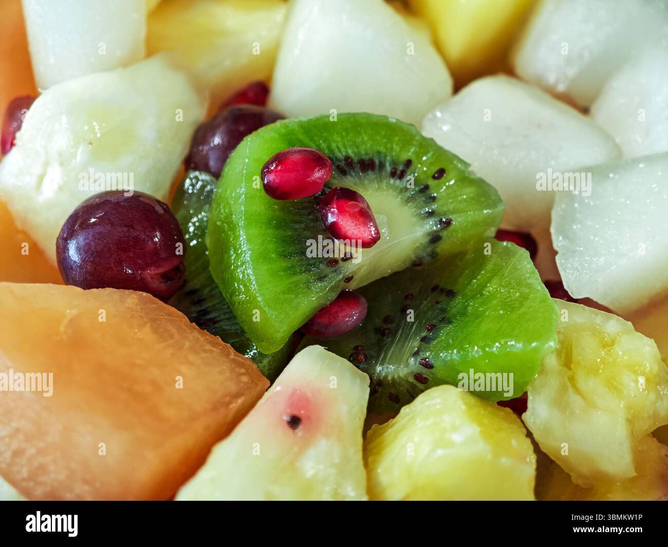 Eine Obstschale mit Kiwi, Trauben, Melone, Ananas und Granatäpfeln. Die Früchte werden gehackt und die Granatäpfel werden in der Schüssel verteilt. Stockfoto