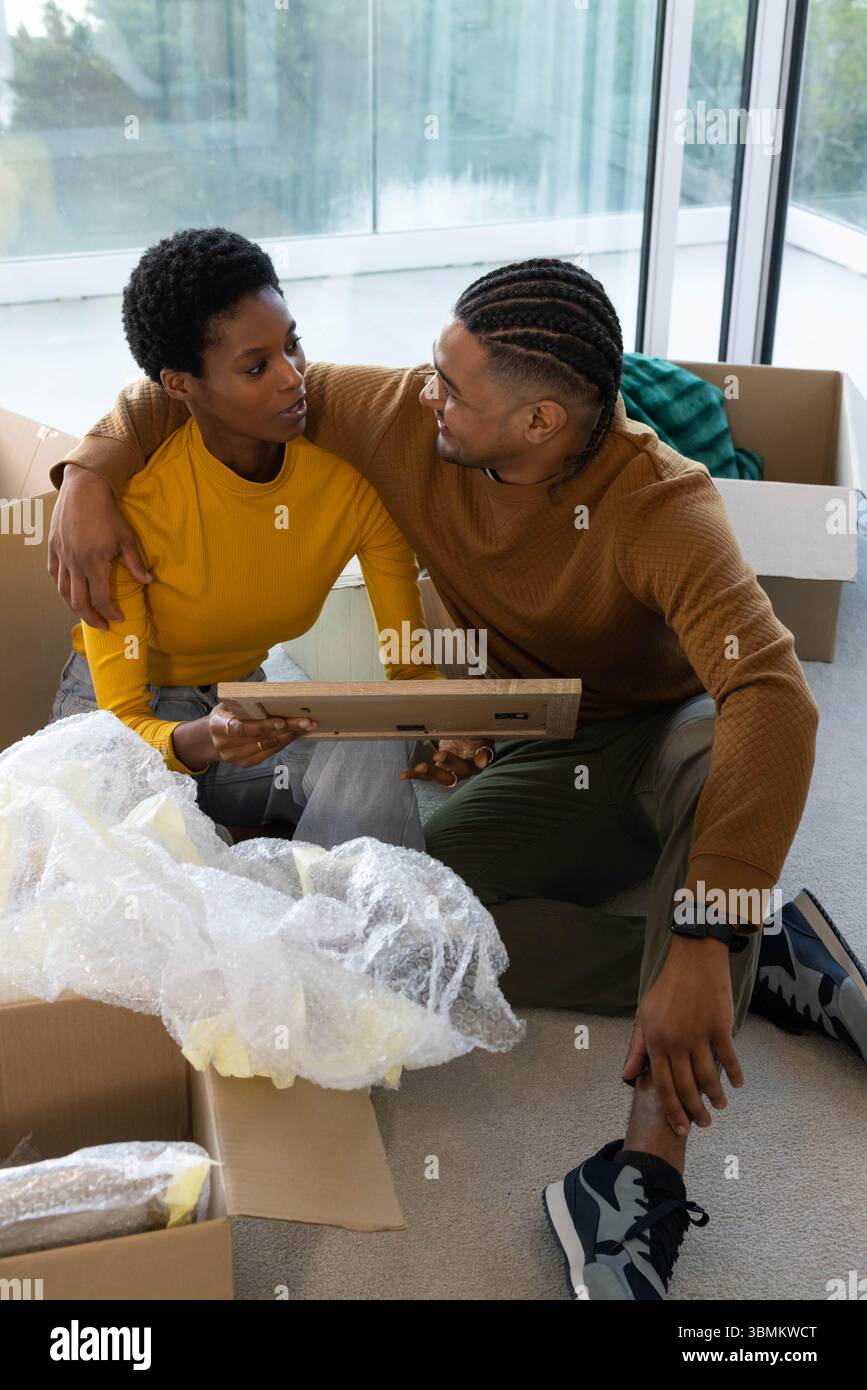 Auspacken diverser Paare, die einen Bilderrahmen auf Teppichboden im Wohnzimmer untersuchen, mit Umzugskartons Stockfoto