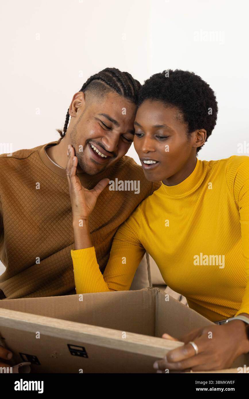 Das aufklappende Paar untersucht den Inhalt der Schachtel auf dem Sofa, trägt ein braunes Stepphemd und einen gelben Rollkragenkragen Stockfoto