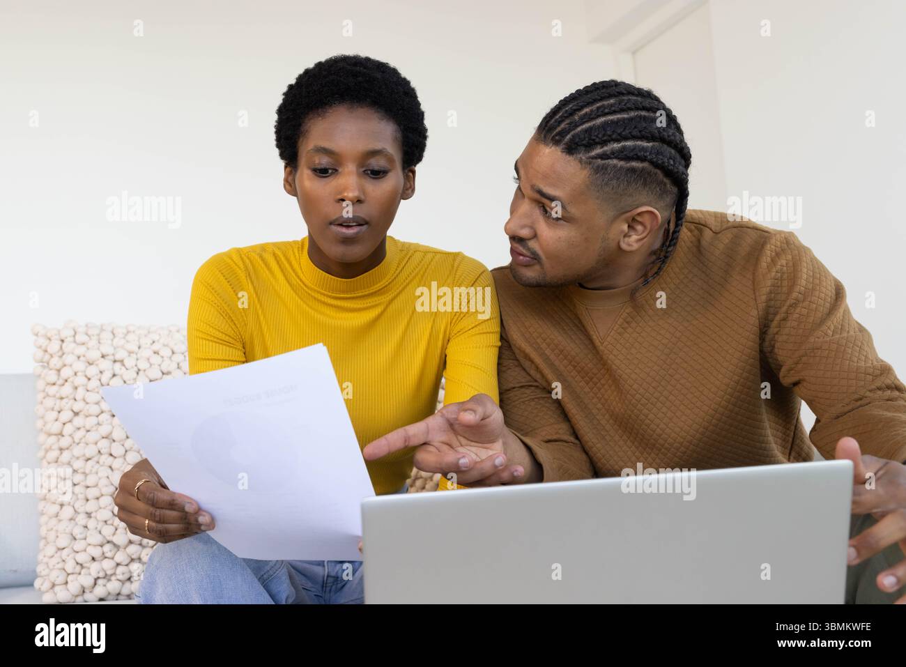 Ich überprüfe das gedruckte Dokument, verschiedene Paare sitzen auf Sofa im Wohnzimmer, mit silbernem Laptop Stockfoto