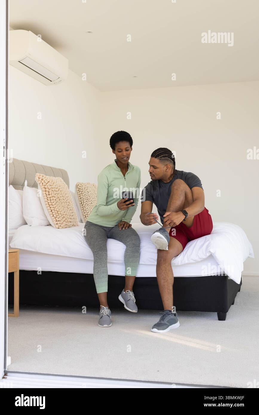 Ein afroamerikanisches Paar in Sportbekleidung sitzt auf dem Bett, mit Sneaker-Schnürsenkeln Stockfoto
