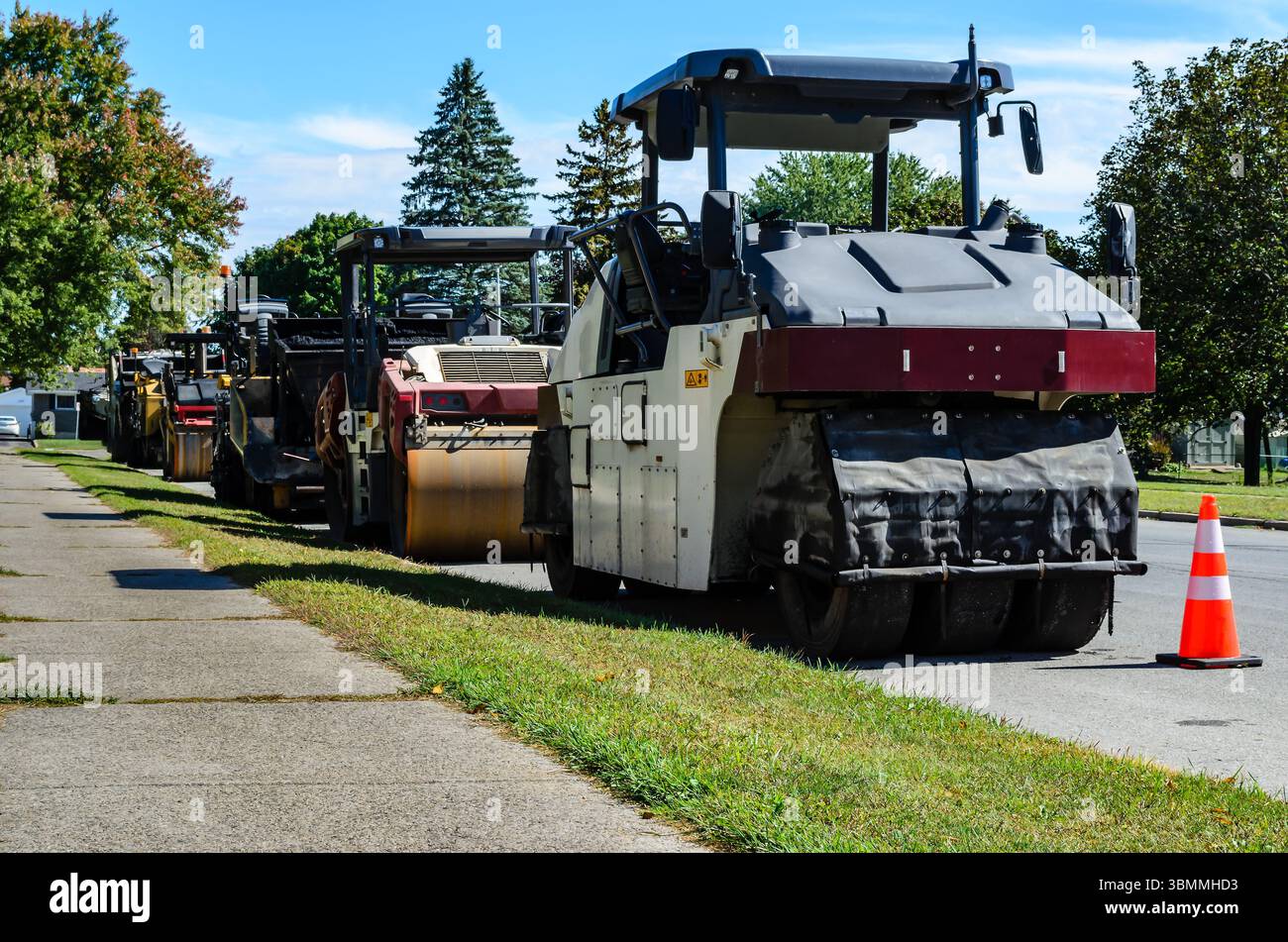 Zahlreiche Baumaschinen parkten im Sommer in einer Reihe entlang einer Wohnstraße Stockfoto