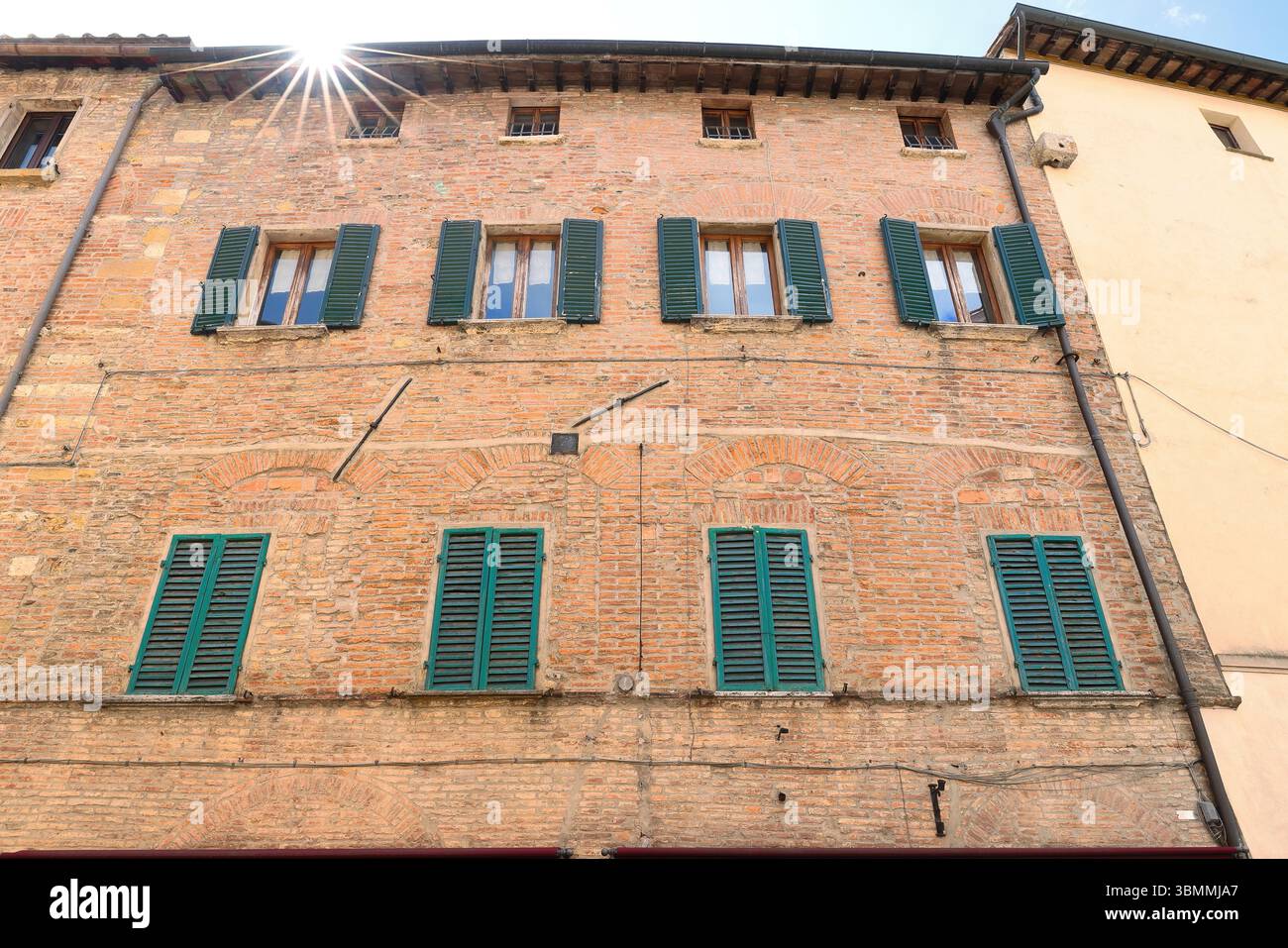 026 Sonnenstern oder Beugungsspitzen, die vom Dach eines roten Ziegelgebäudes mit grünen Holzläden ausstrahlen. Montepulciano-Toskana-Italien. Stockfoto
