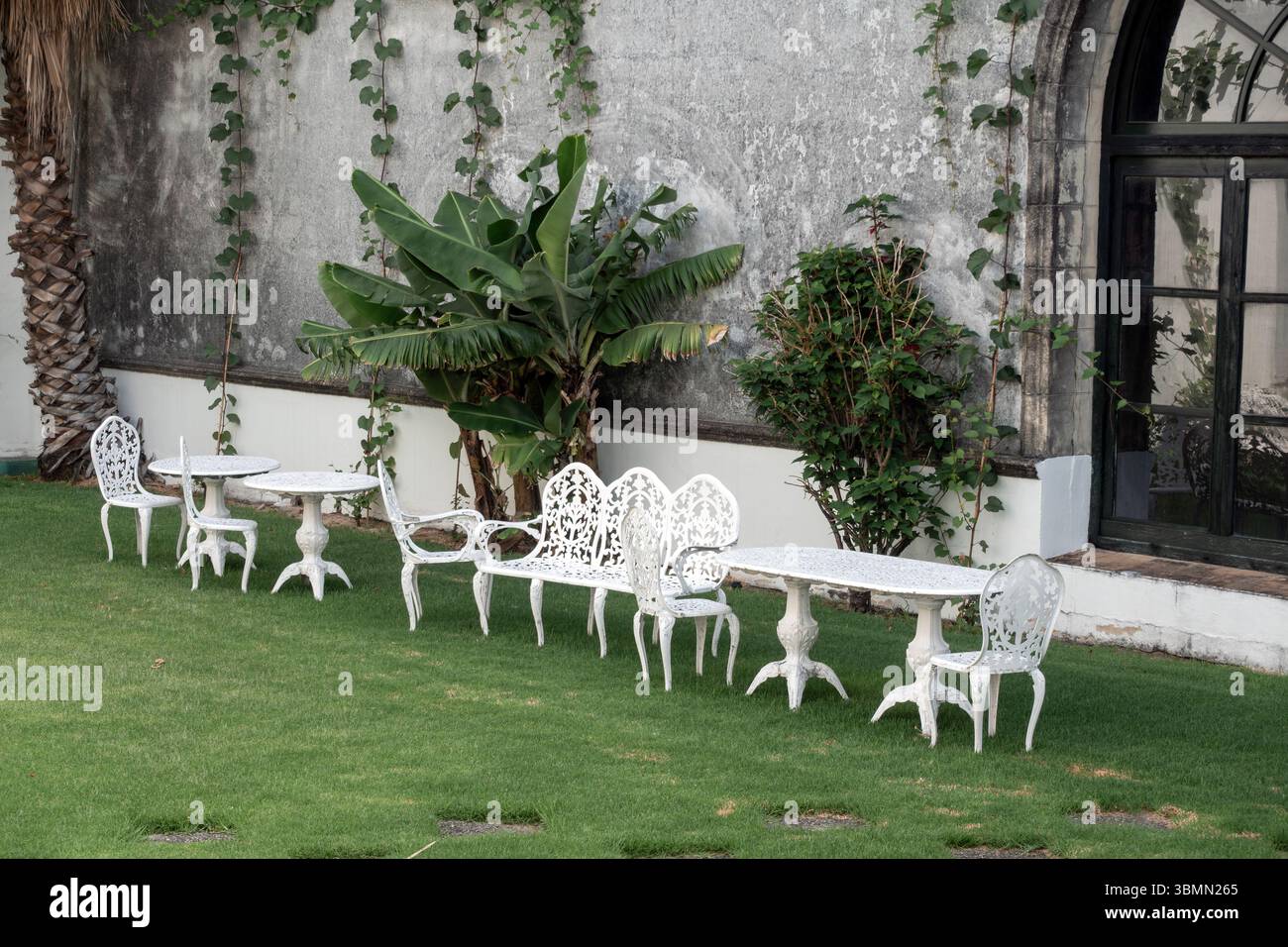 Ein bezaubernder Garten mit Retro-Elementen – schmiedeeiserne Möbel, weiche Pastellfarben und blühende Blumen erinnern an zeitlose Schönheit und entspannte Eleganz. Stockfoto