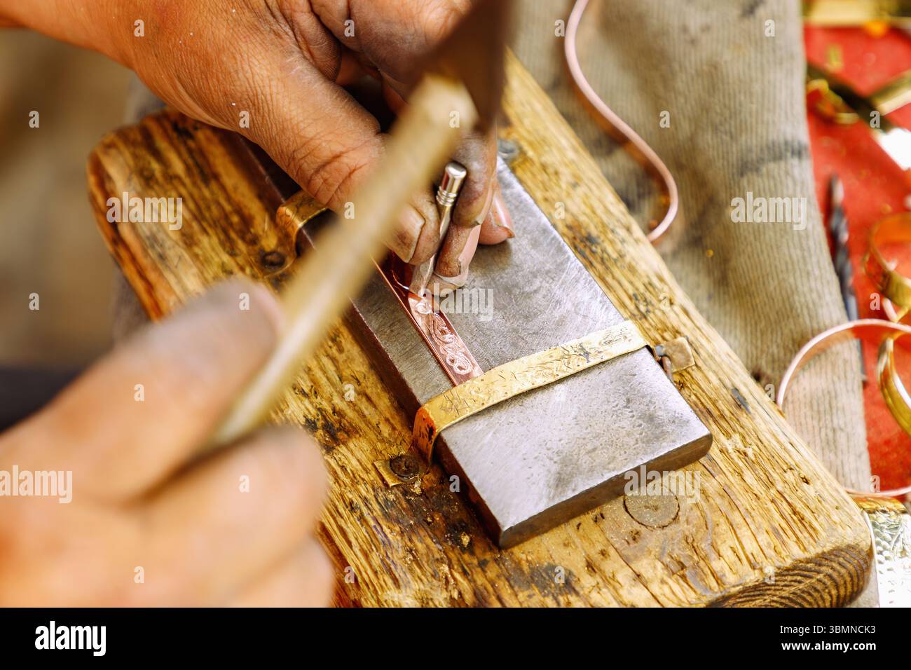 Handwerker graviert ein Kupferarmband mit einem traditionellen Gravurwerkzeug im Souk in der Medina von Nabeul, Tunesien Stockfoto