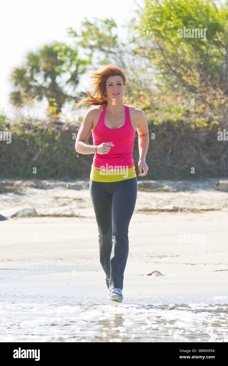 Eine junge, fitte Brünette läuft an einem schönen Sommermorgen am Strand entlang und erwärmt ihre Haut, während sie sich mit Energie und Freiheit gegen die B bewegt Stockfoto