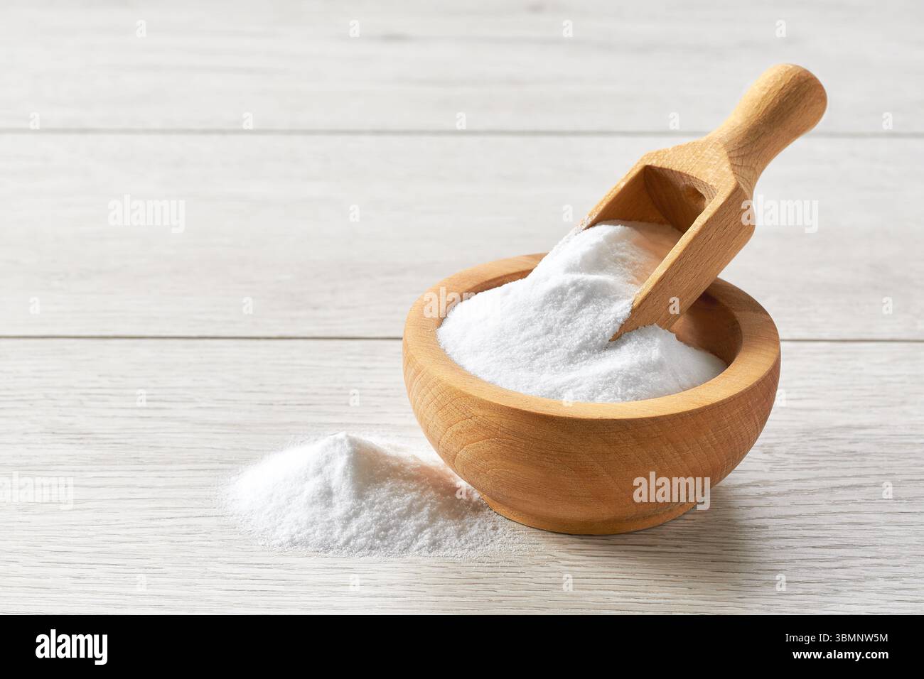 Backpulver in Holzlöffel und Schüssel auf einem hellen Holztisch. Stockfoto