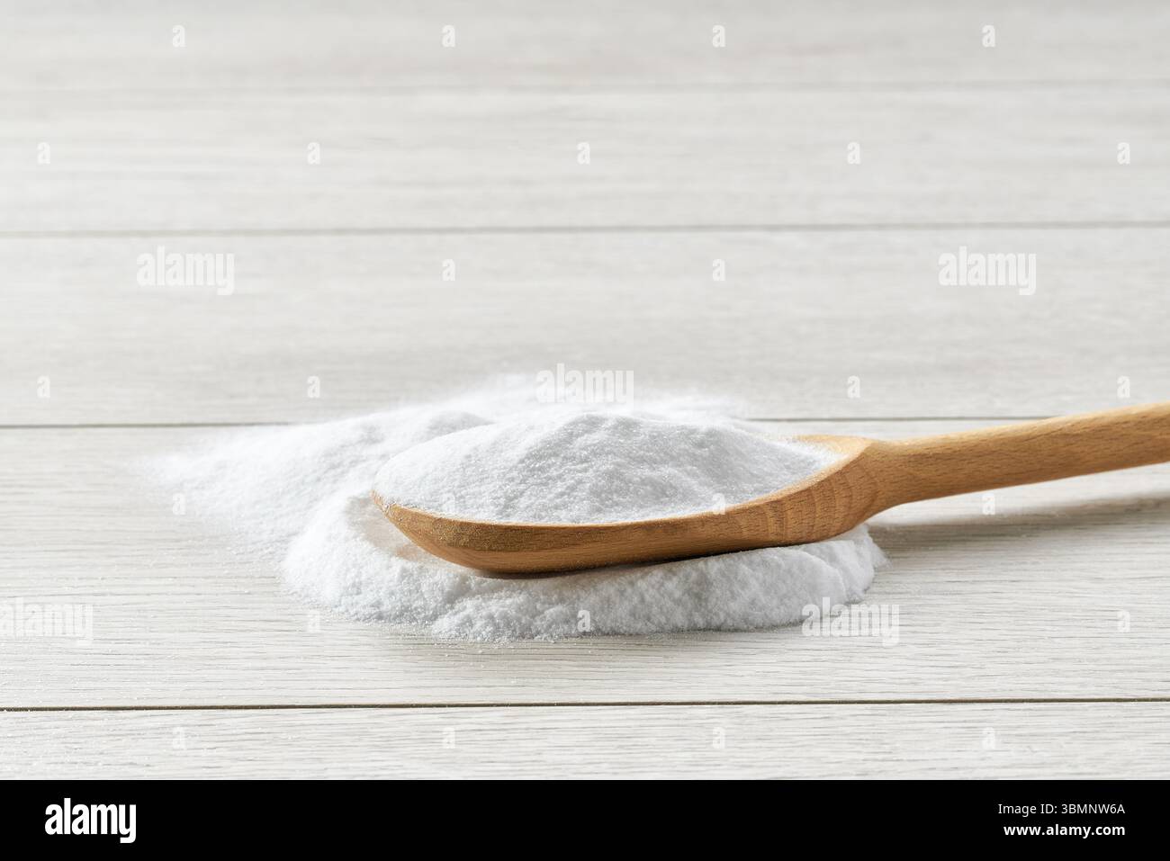 Backpulver in einem Holzlöffel auf einem weißen Holztisch. Stockfoto