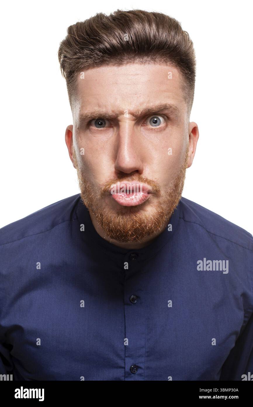 Attraktiver junger bärtiger Mann mit blauem Hemd macht Gesichter, isoliert auf weißem Hintergrund Stockfoto