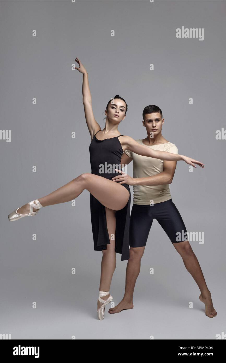 Zwei anmutige Balletttänzer posieren über einem grauen Studiohintergrund und schauen in die Kamera. Hübscher Mann in schwarzen Shorts mit beigem T-Shirt Stockfoto