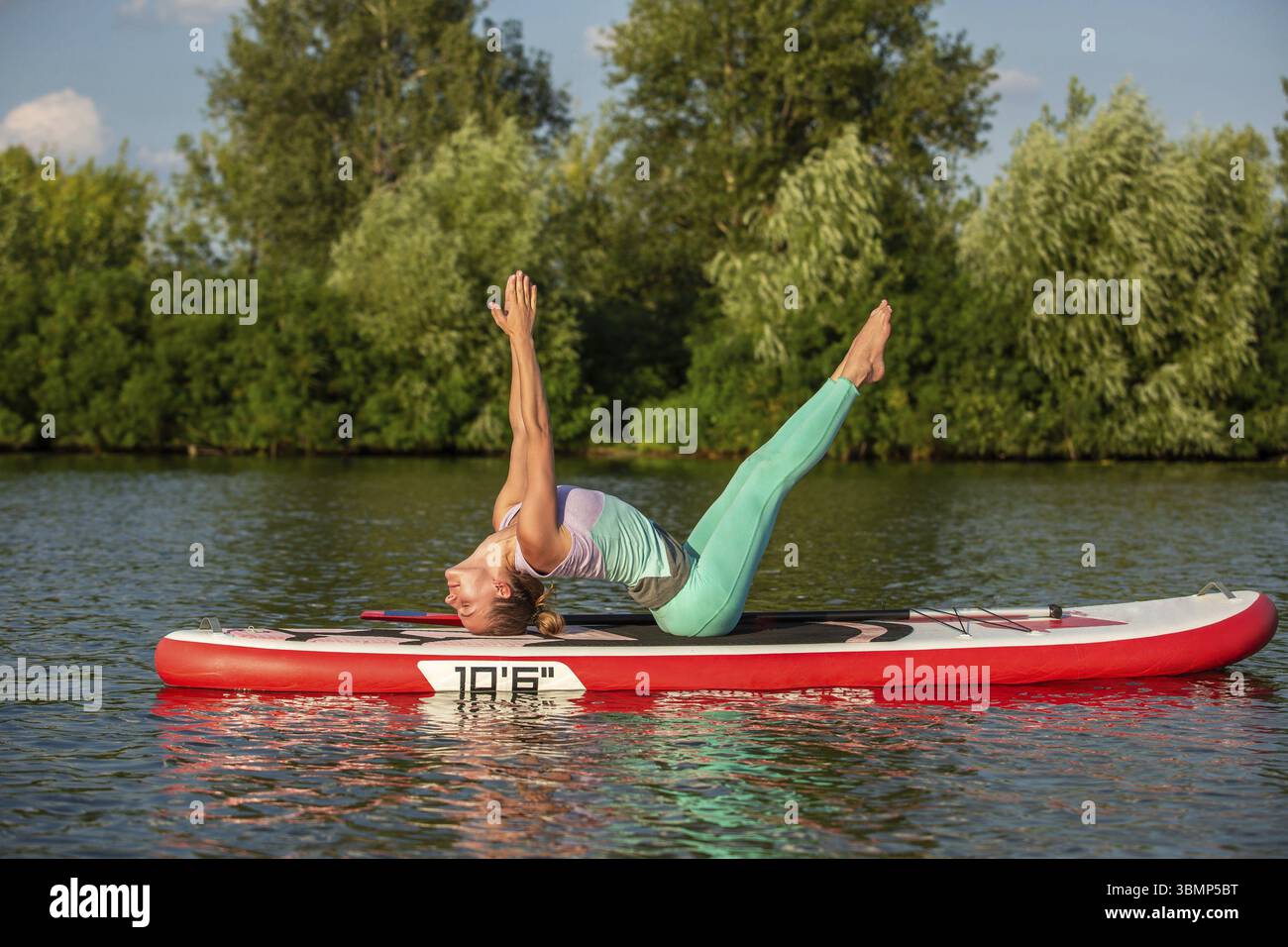 Junge Frau Yoga auf dem sup Board mit Paddeln. Yoga Pose, Seitenansicht - Begriff der Harmonie mit der Natur, frei und gesund leben, freiberuflich, Remote Stockfoto