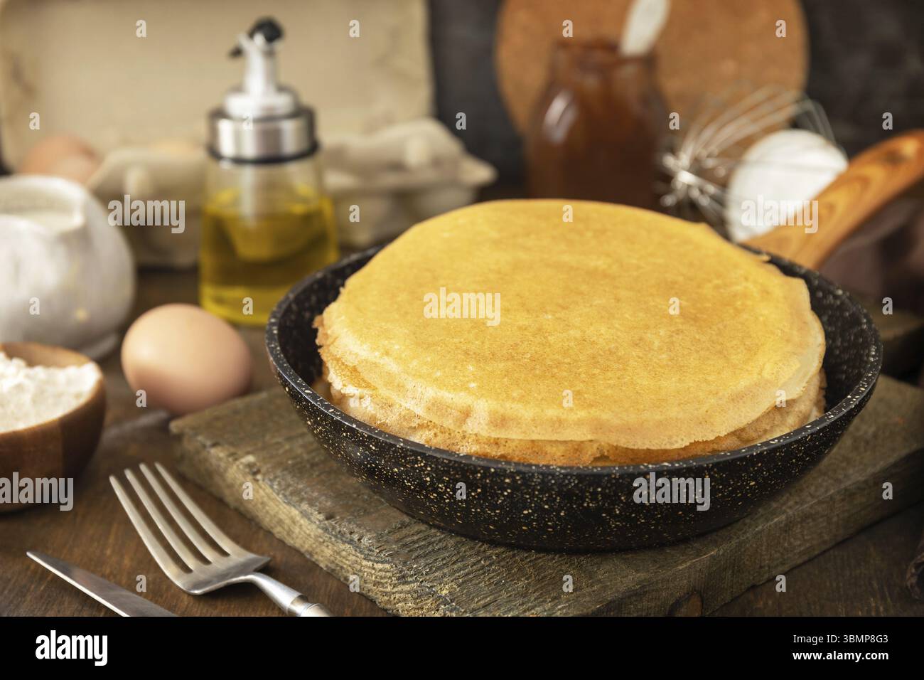 Pancake Day feiern, gesundes Frühstück kochen. Köstliche hausgemachte Crepes oder Pfannkuchen in einer Pfanne und Zutaten auf einem rustikalen Tisch Stockfoto