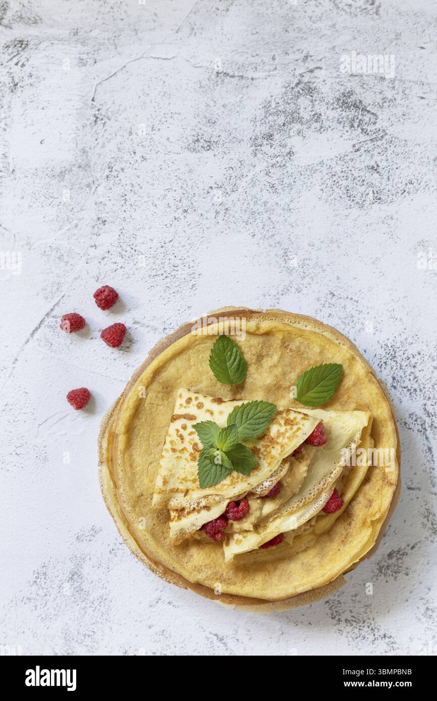 Gesundes Frühstück, Pancake Day. Köstliche hausgemachte Crepes mit Himbeeren und Erdnusspaste auf einer Steinplatte. Draufsicht flach. Kopie sp Stockfoto