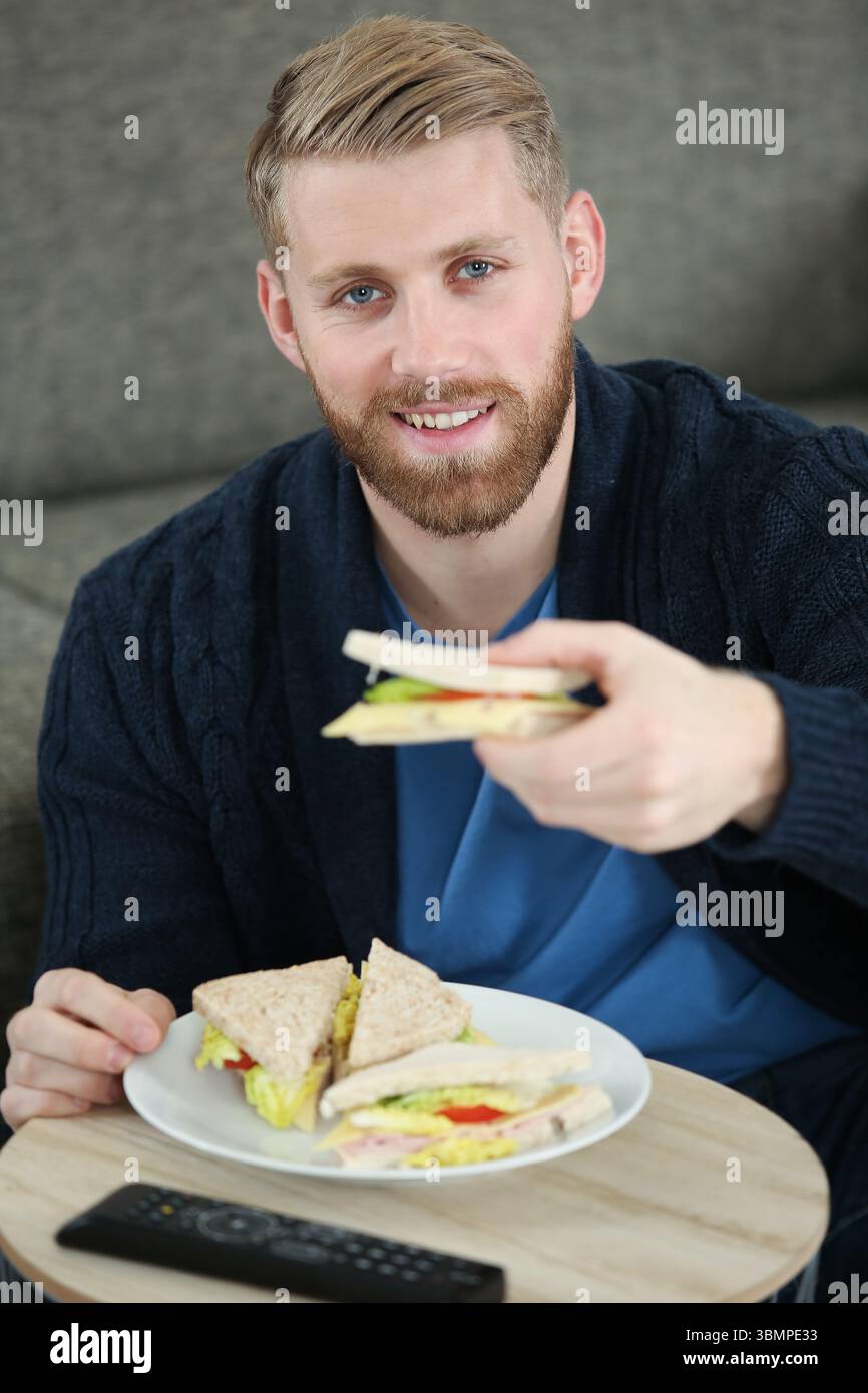 Junger Mann, der zu Hause leckeres Sandwich isst Stockfoto