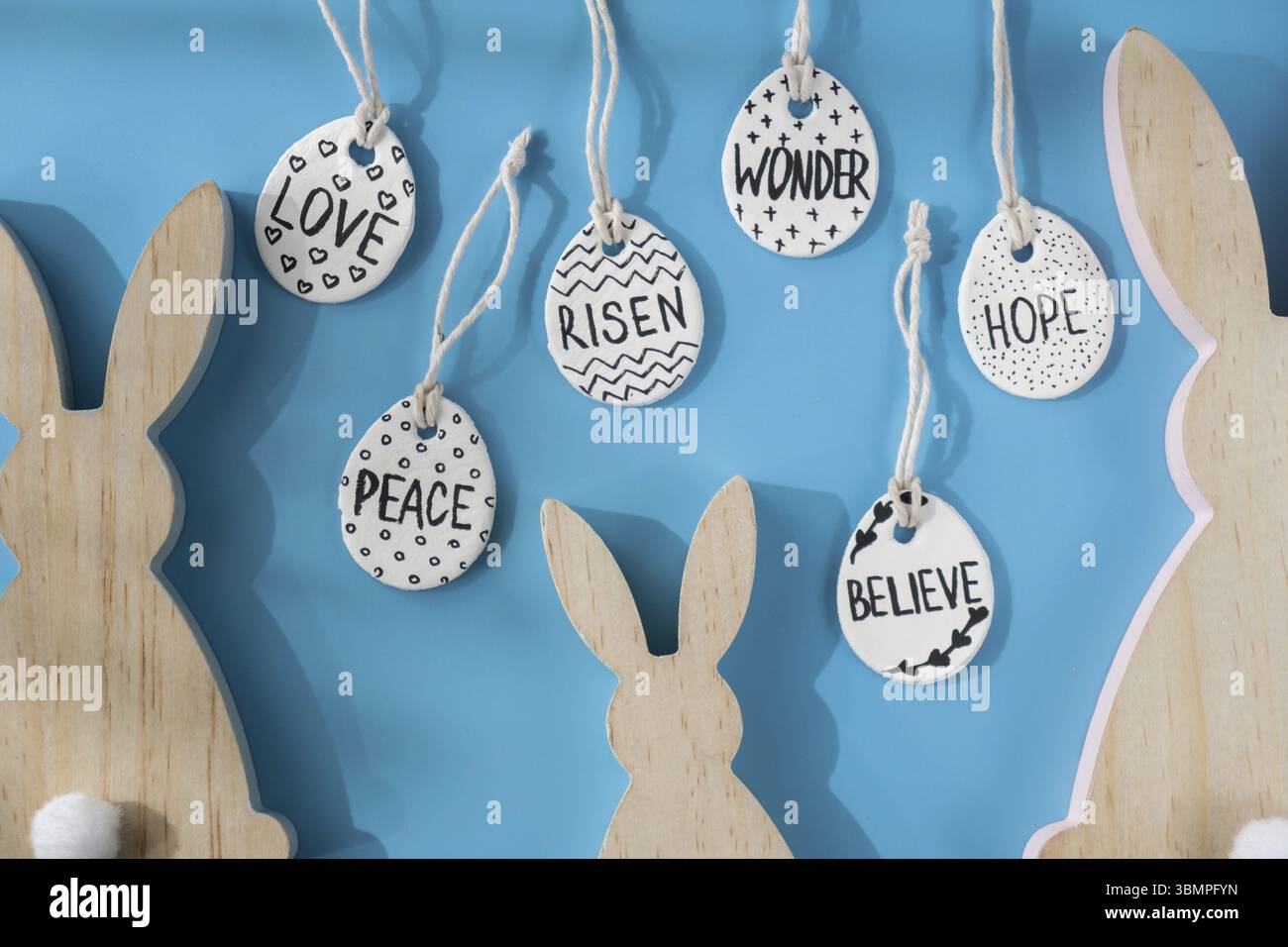 Gruppe von hölzernen Hasenohren und Ton Ostereiern mit den Worten AUFERSTANDEN HOFFNUNG GLAUBEN FRIEDEN LIEBE WUNDER tun Sie es selbst lufttrockene Lehm Handwerk für die Osterferien. Stockfoto