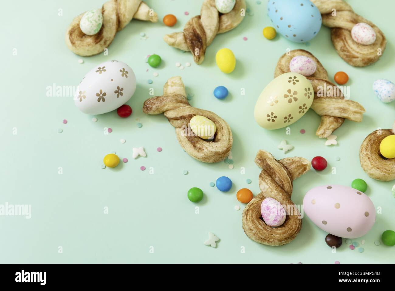 Farben Ostereier mit Osterkaninchen-förmigen Brötchen Blätterteig mit Zimt auf pastellgrünem Hintergrund. Frohe Osterferien Stockfoto