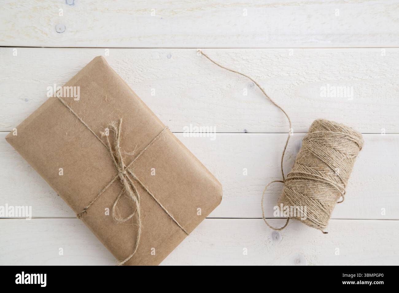 Paket, Geschenk verpackt in umweltfreundlichem Papier und Garn zum Verpacken auf hellem Holzhintergrund. Die Aussicht von oben Stockfoto
