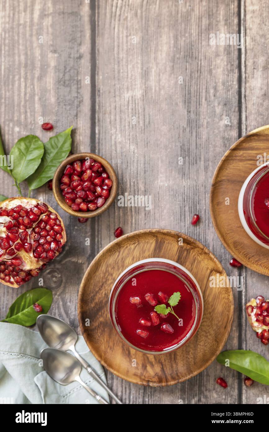 Winter köstliches italienisches Dessert Panna Cotta mit Granatapfelgelee und Minze, hausgemachte Küche auf hölzernem Hintergrund. Blick von oben. Kopierbereich Stockfoto