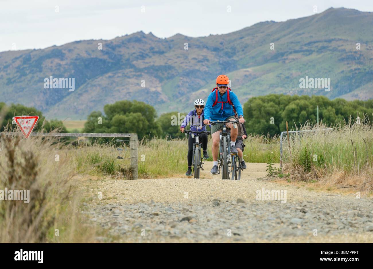 Paare, die auf der Schotterpiste fahren. Schild am Zaun geben. Otago Central Rail Trail. Südinsel. Neuseeland. Stockfoto