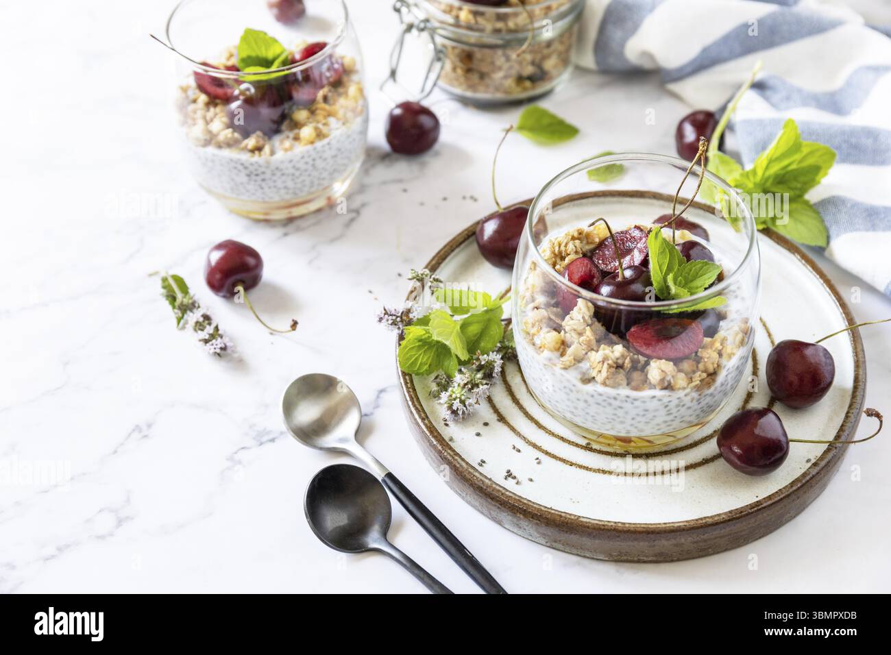 Gesundes Menükonzept. Hausgemachtes Müsli-Frühstück. Glas Parfait aus Müsli, Beerenkirsche, Joghurt mit Chiasamen auf rustikalem Tisch. Kopieren Sie den SPAC Stockfoto
