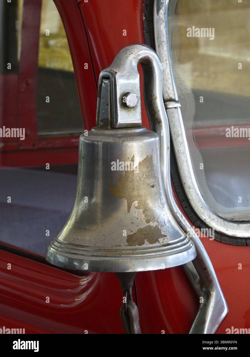 Nahaufnahme einer glänzenden Metallglocke, die an einem knallroten Feuerwehrauto befestigt ist und Zeichen von Alter und Verschleiß zeigt Stockfoto