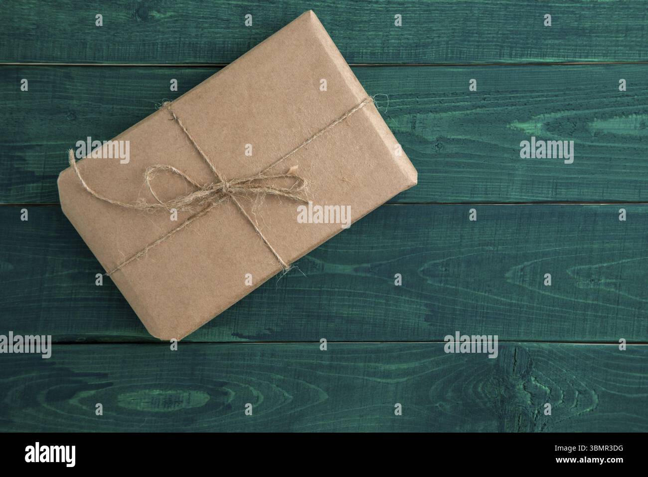 Paket, Geschenk verpackt in umweltfreundlichem Papier auf dunkelgrünem Holzhintergrund. Die Aussicht von oben Stockfoto