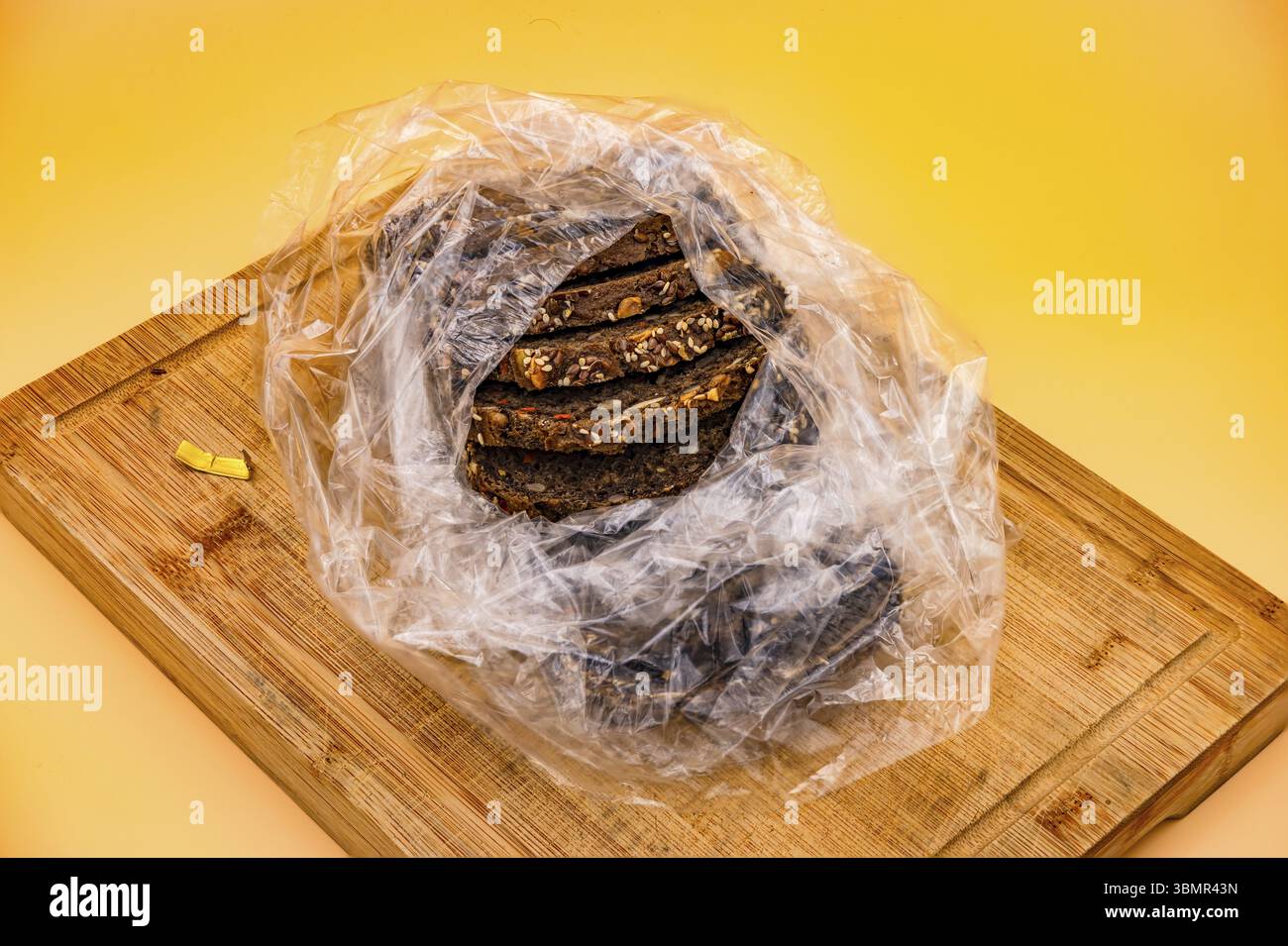Frisch gebackenes Vollkornbrot in einer Plastiktüte geschnitten, fotografiert auf einem Schneidebrett vor gelbem Hintergrund im Studio Stockfoto