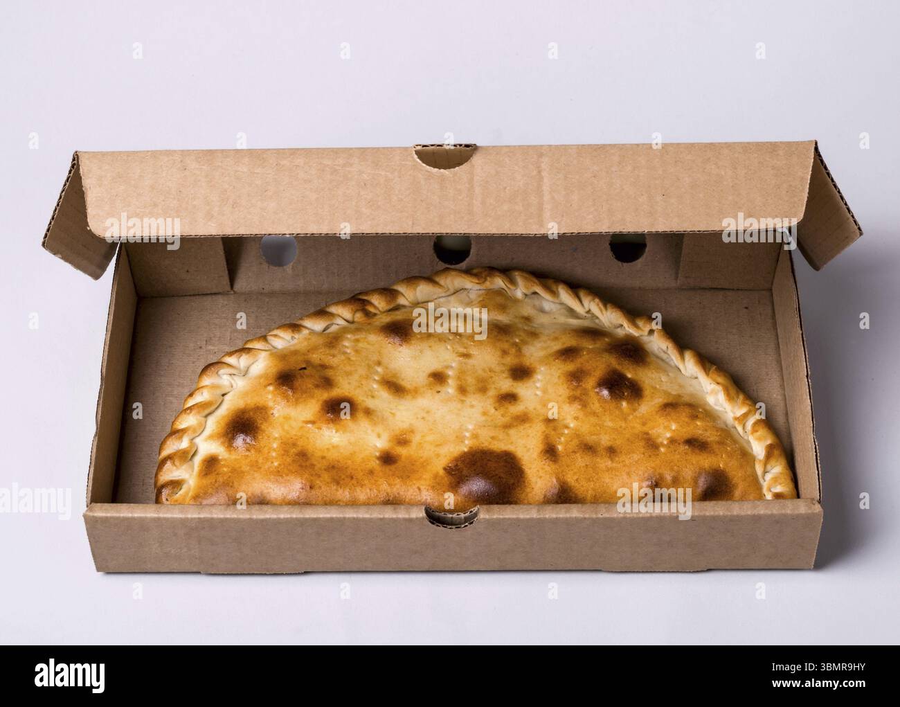 Geschlossene Pizza-Calzone in Packbox auf grauem Hintergrund Stockfoto