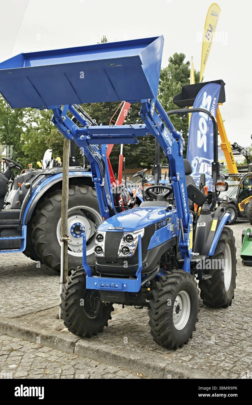 Kleiner blauer Solis-Traktor mit Frontlader, der während der Landmaschinenausstellung auf der Kopfsteinpflasterstraße geparkt wurde Stockfoto