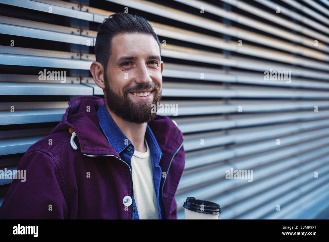 Im Herbst oder Winter Portrait von Stattlichen hipster Mann mit Bart, weisses T-Shirt, blau Shirt und kastanienbraunen Jacke Holding heiße Tasse Kaffee. Gerippte urba Stockfoto