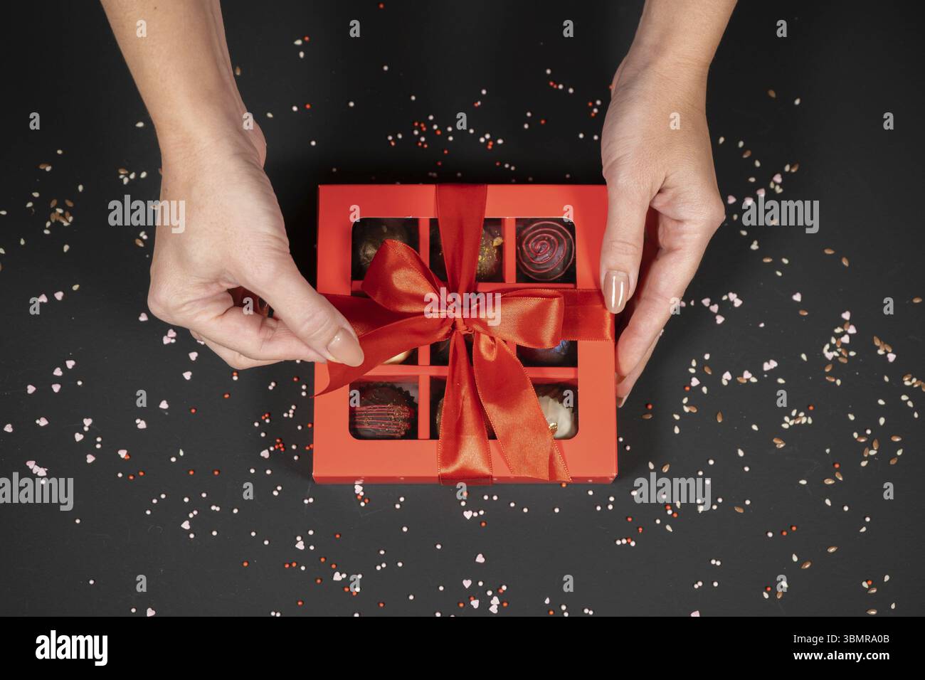 Verschiedene handgemachte Schokoladentrüffel-Bonbons in einer roten Box auf dunklem Hintergrund in weiblichen Händen Stockfoto