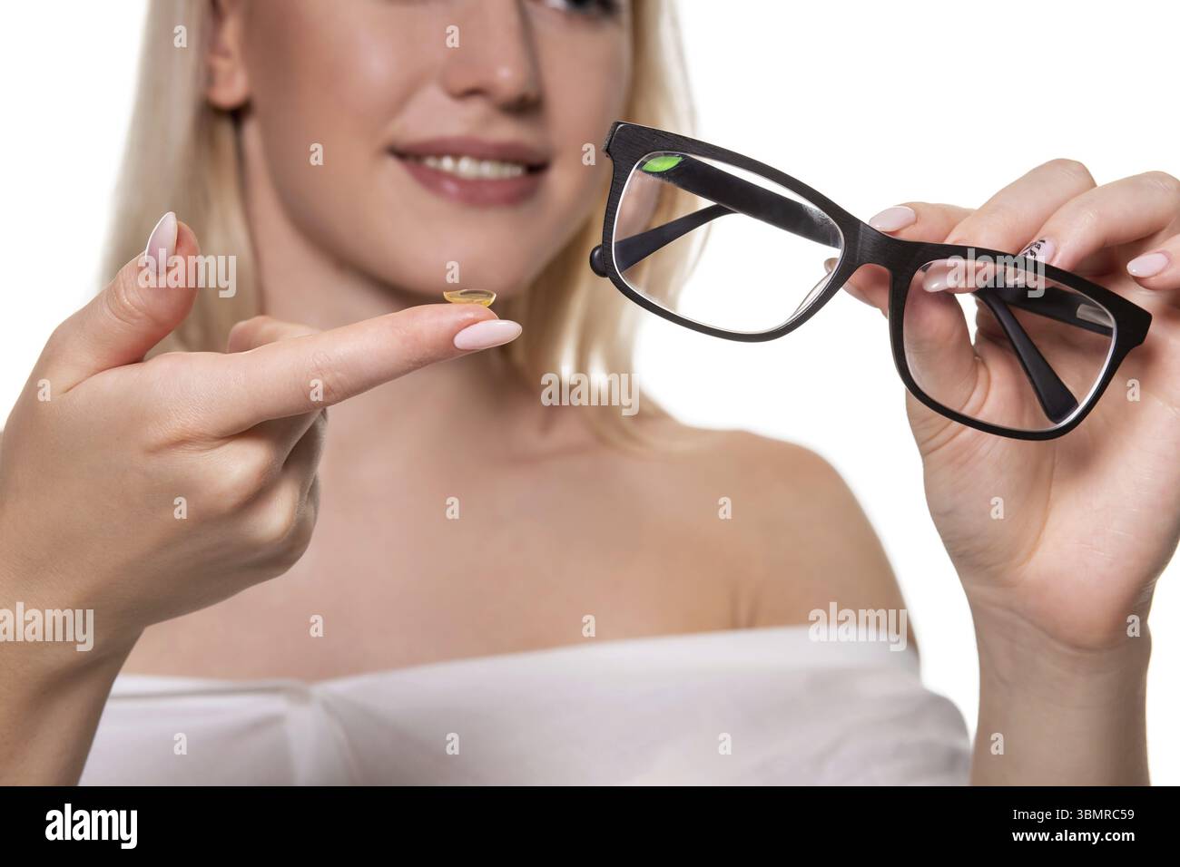 Junge blonde Frau mit Kontaktlinsen auf den Finger vor ihrem Gesicht und halten in der anderen Hand eine schwarze Brille auf weißem Hintergrund. Close-up. Ey Stockfoto