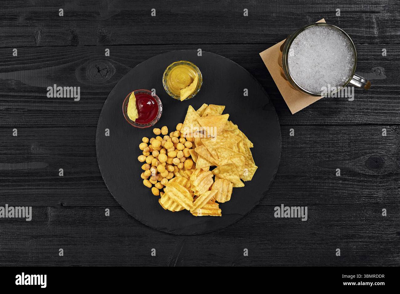 Blick von oben auf Bierglas und Snacks mit Sauce auf schwarzem Holztisch. Draufsicht. Speicherplatz kopieren. Stillleben. Flach liegend Stockfoto