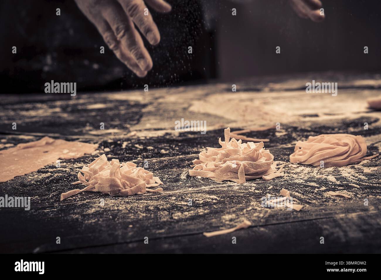 Der Koch bereitet frische Spaghetti von Grund auf zu. Holztisch. Foto in Brauntönen. Küche Stockfoto