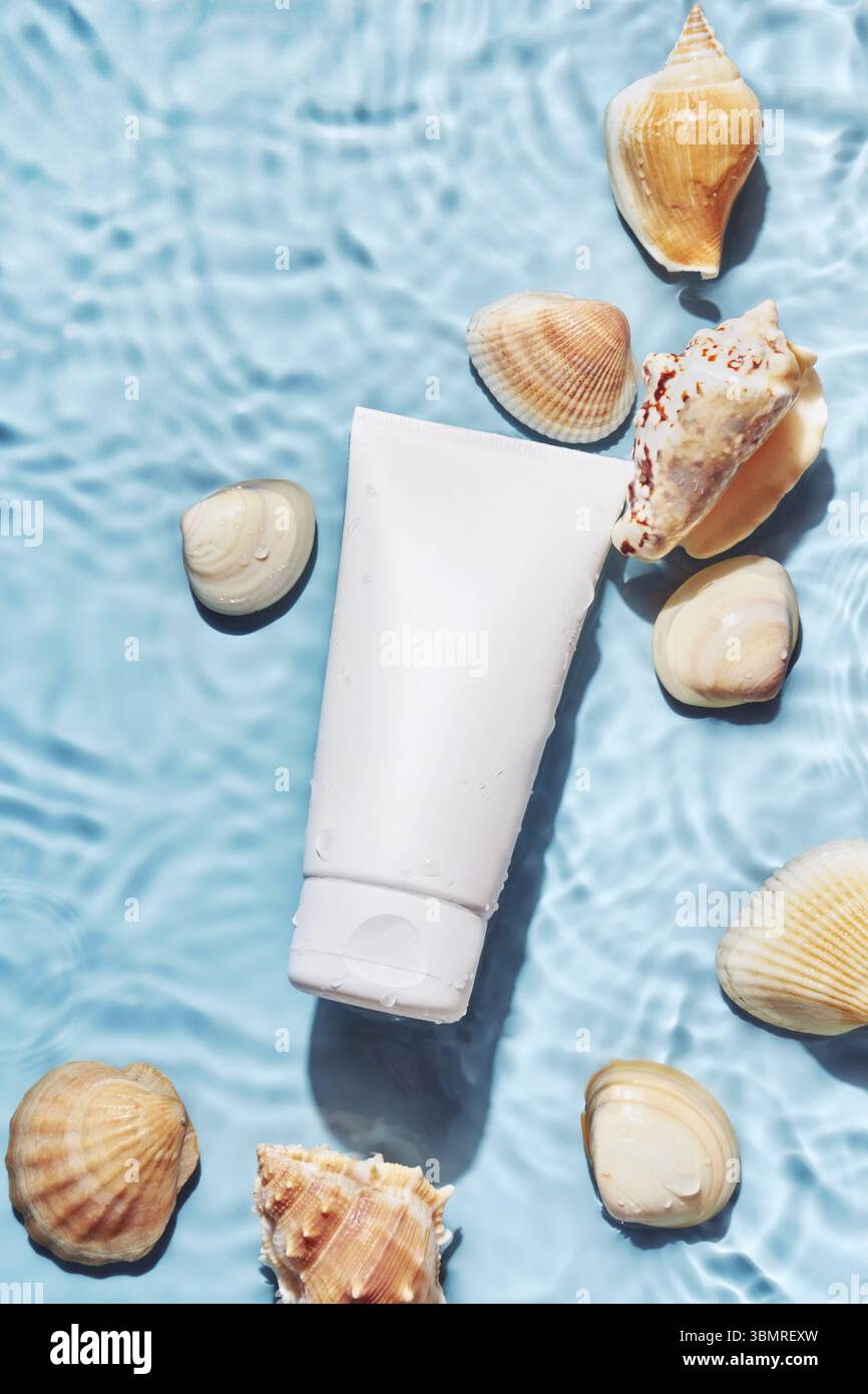 Organisches Kosmetikprodukt mit Meeresmineralien. Hautpflegecreme oder Sonnenschutz und Schalen auf blauem Wasserhintergrund Stockfoto