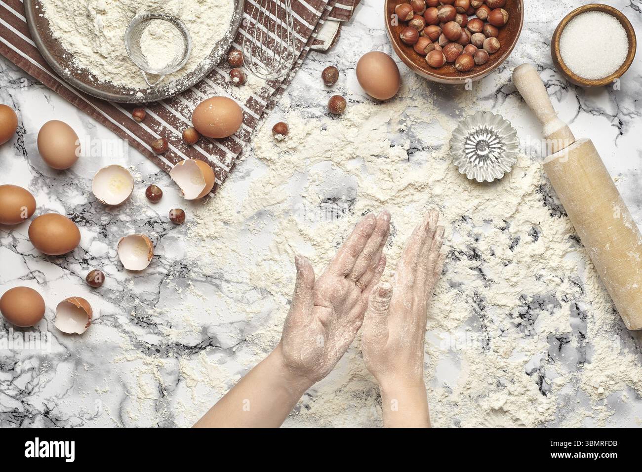 Nahaufnahme. Blick von oben auf einen Bäckerplatz, der mit einem rohen Teig, Backzutaten und Küchenutensilien auf dem Marmortisch arbeitet. Hände des Küchenchefs Stockfoto