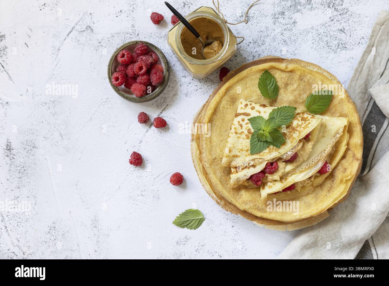 Gesundes Frühstück, Pancake Day. Köstliche hausgemachte Crepes mit Himbeeren und Erdnusspaste auf einer Steinplatte. Draufsicht flach. Kopie sp Stockfoto