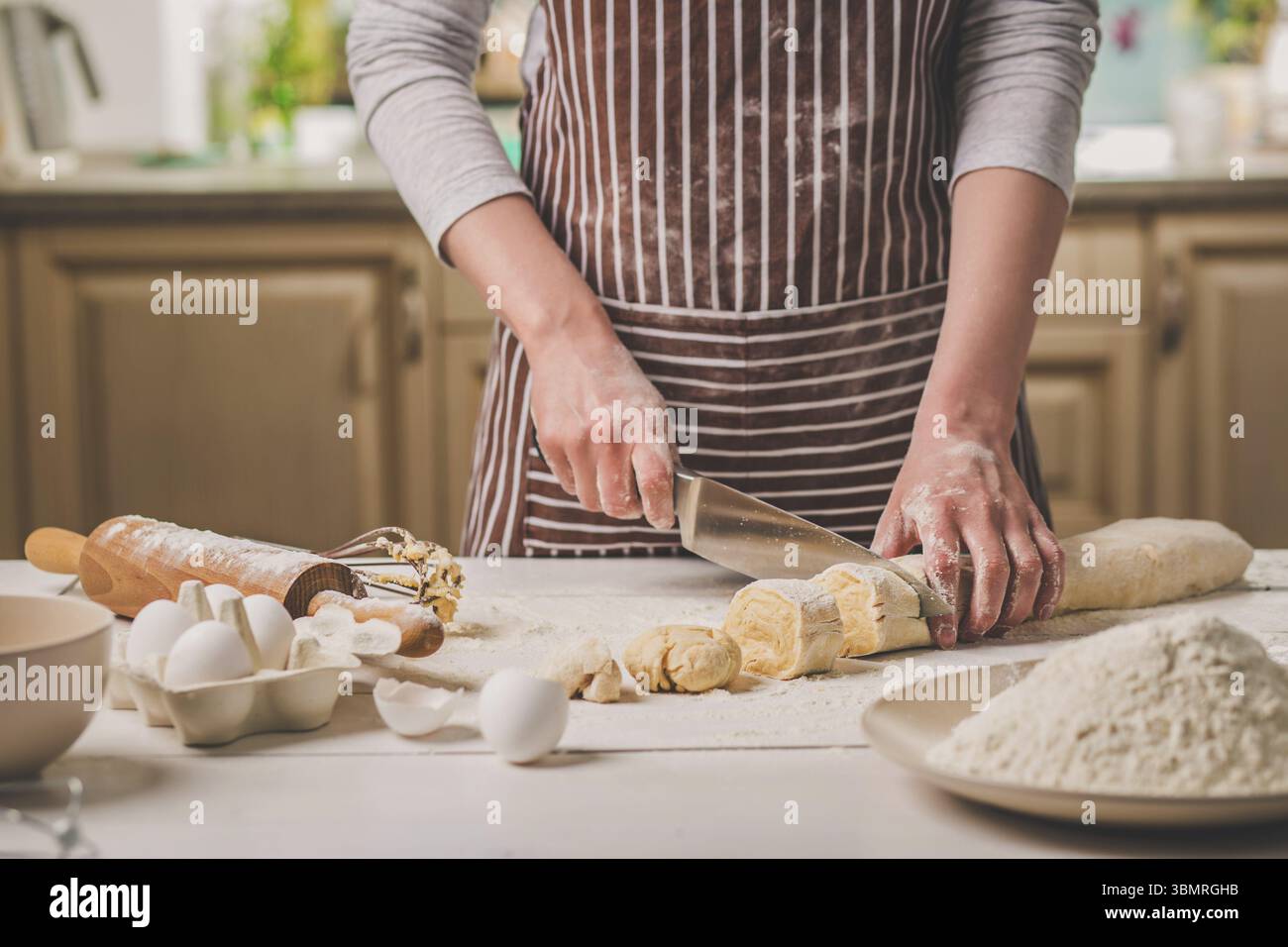 Nahaufnahme der beiden Frau Hände schneiden Messer Teig. Eine Frau in einem gestreiften Schürze ist das Kochen in der Küche Stockfoto