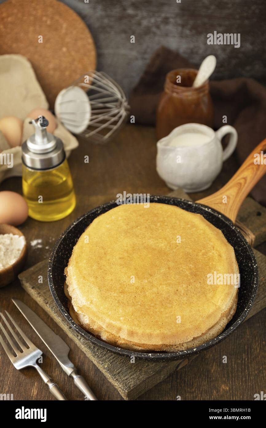 Pancake Day feiern, gesundes Frühstück kochen. Köstliche hausgemachte Crepes oder Pfannkuchen in einer Pfanne und Zutaten auf einem rustikalen Tisch Stockfoto
