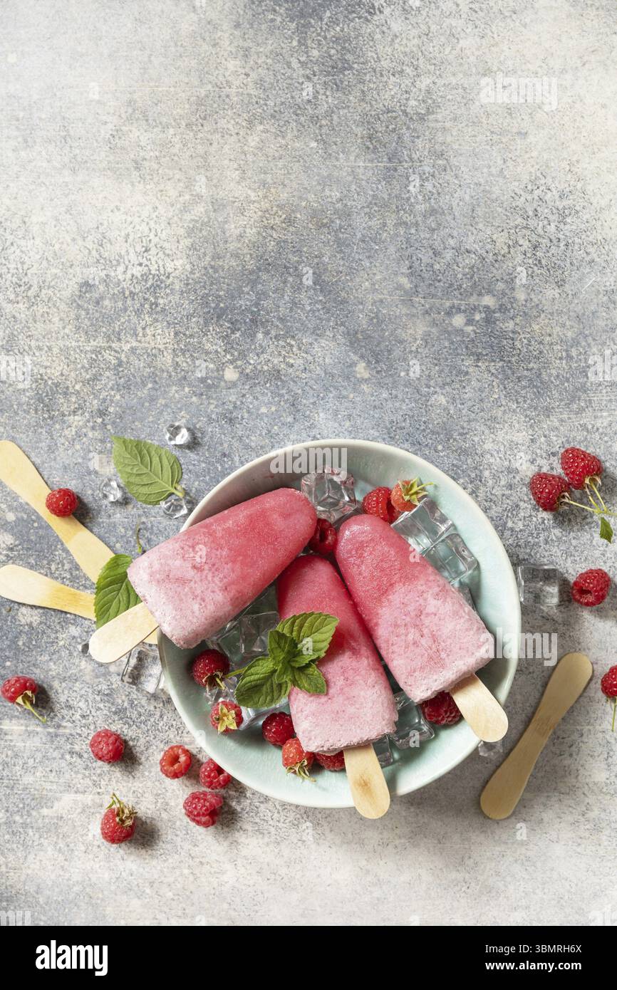 Hausgemachte Himbeergelenke mit Joghurt und Himbeeren auf grauem Steinhintergrund. Eis. Sommerdessert. Blick von oben. Kopierbereich Stockfoto