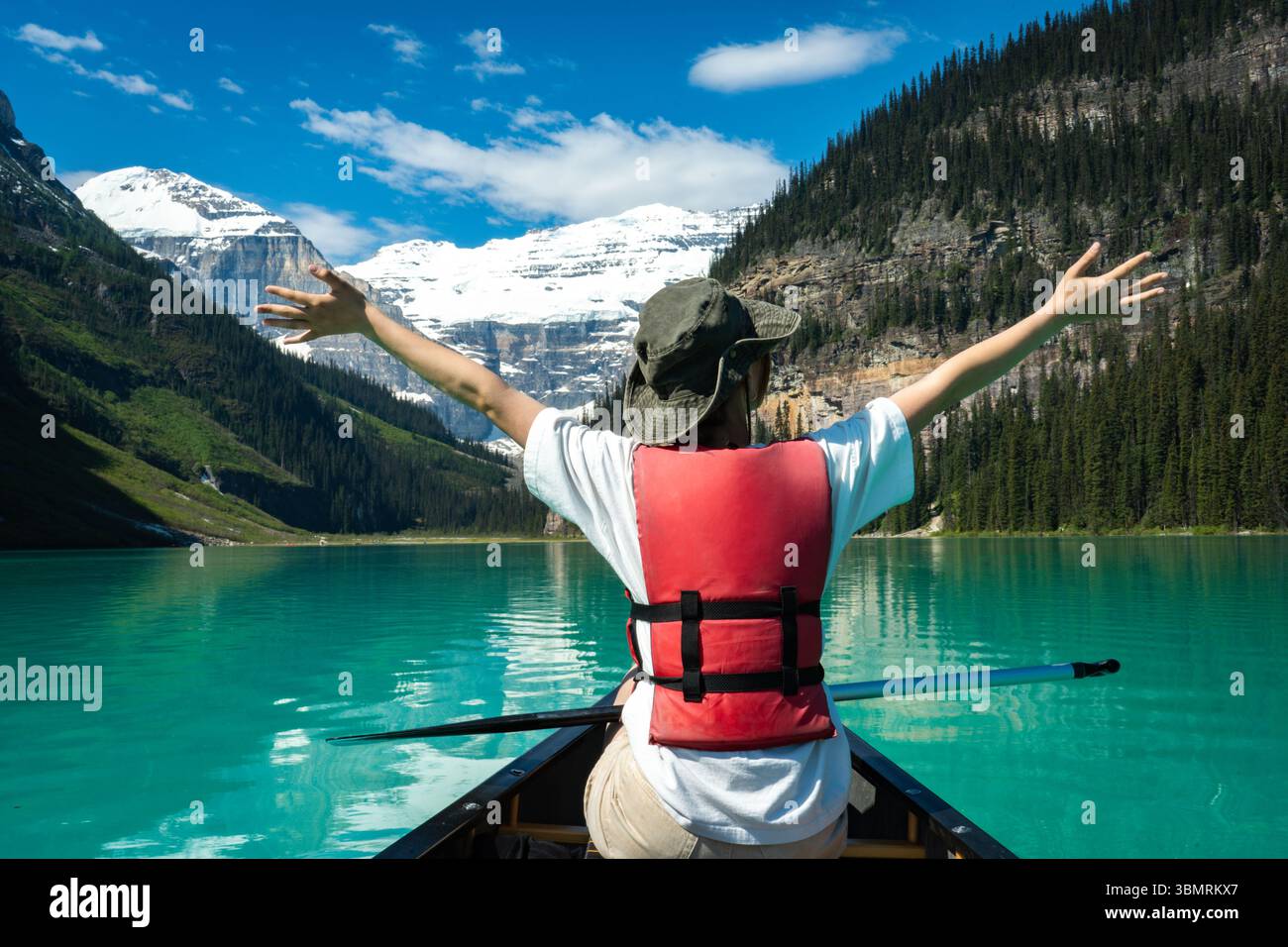 Person mit freudig erhobenen Armen auf dem Kanu in atemberaubender Bergsee-Landschaft. Stockfoto