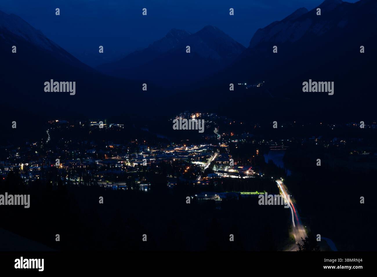 Die Stadt wird nachts unter dunklen Berglandschaften in einem Tal beleuchtet Stockfoto